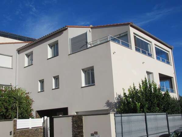 Um edifício moderno de dois andares com telhado plano, várias janelas e entrada com portão.