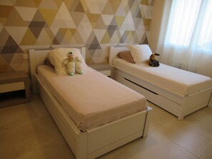 Quarto com duas camas, parede com padrão geométrico e janela com cortinas translúcidas.