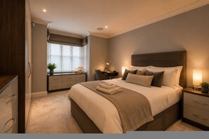 Ein Schlafzimmer mit einem großen Bett, Nachttischen, einem Schreibtisch und einem Stuhl. Es gibt ein Fenster mit Jalousien.