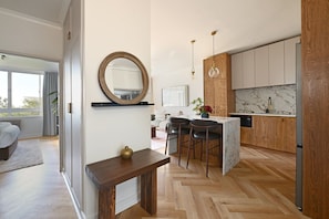 A modern kitchen with wooden cabinets, a marble backsplash, and a central island with bar stools. - Two Bed Green Point Secure Designer Apartment (Cape Town)