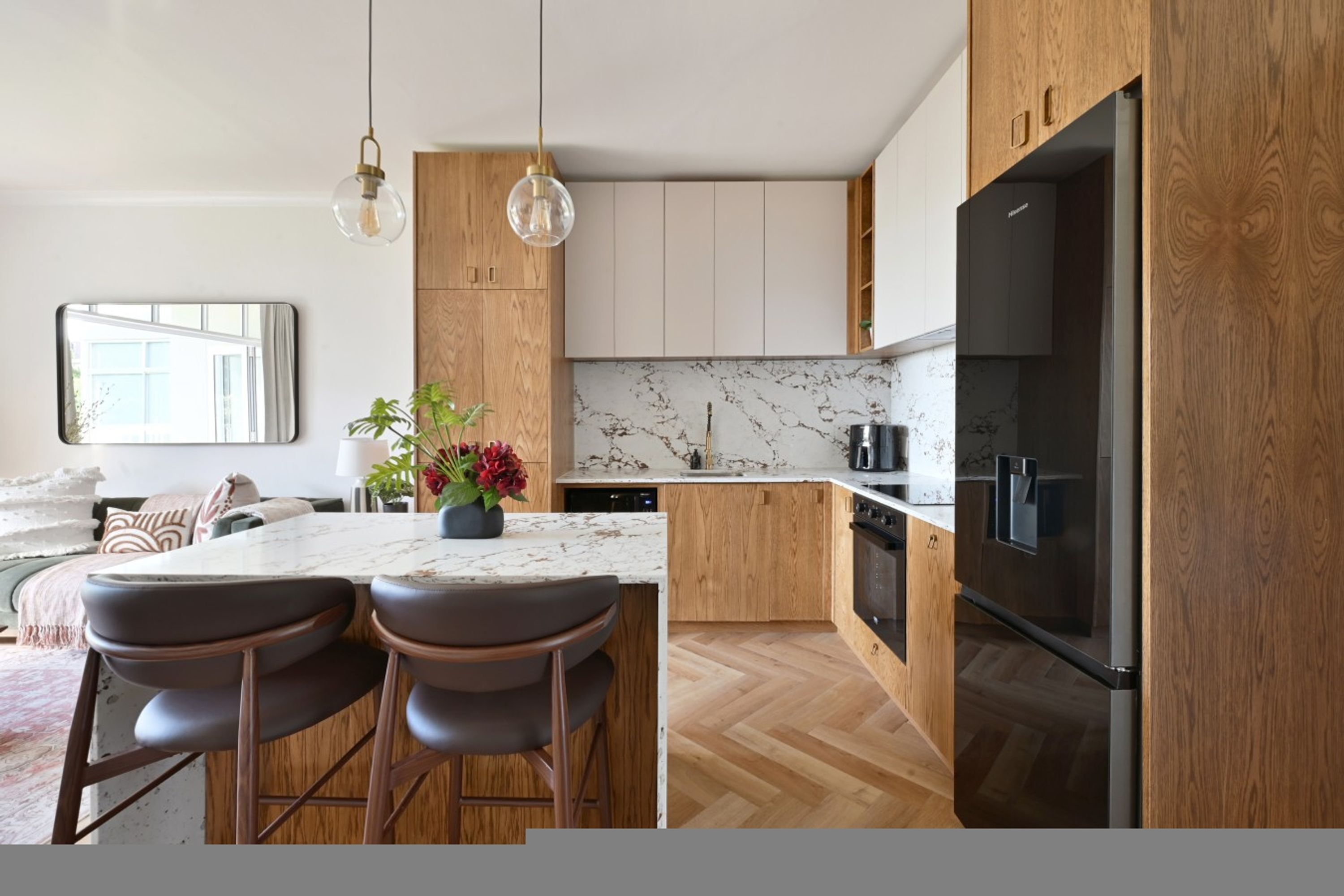 A modern kitchen with wooden cabinets, a marble backsplash, and a large black refrigerator.