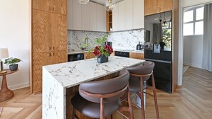 Una cocina moderna con gabinetes de madera, una isla de mármol y taburetes de bar.