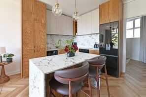 A modern kitchen with wooden cabinets, a marble island, and bar stools. - Two Bed Green Point Secure Designer Apartment (Cape Town)