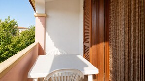 Ein Balkon mit weißem Tisch und Stuhl, einer Holztür und Blick auf Grünflächen.