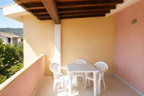 A balcony with a white table and chairs, a wooden ceiling, and a pink wall. - Vrbo Property (Tanaunella, Budoni)