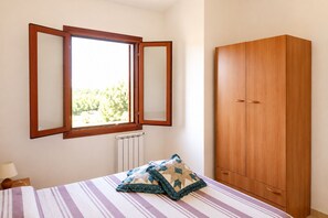 A bedroom with a bed, a window with a view, a radiator, and a wardrobe. - Vrbo Property (Tanaunella, Budoni)