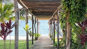 Un chemin pavé de briques mène à une plage, et une pergola en bois est installée au-dessus.