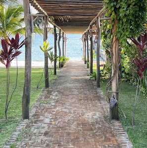 Un sendero de ladrillo que conduce a una playa, con una pérgola de madera sobre él.