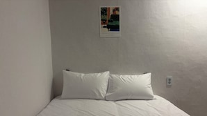 A simple room with a bed, two pillows, a wall-mounted light switch, and a poster on the wall. - StayDucksan Hotel (Suwon)