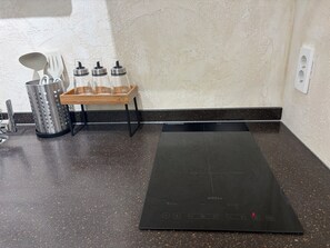 A kitchen with a black induction cooktop, a wooden spice rack, a metal colander, and a white wall.