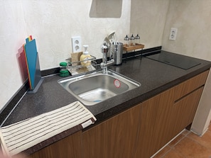 A kitchen with a stainless steel sink, wooden cabinets, a black countertop, and a dish rack with cleaning supplies. - StayDucksan Hotel (Suwon)