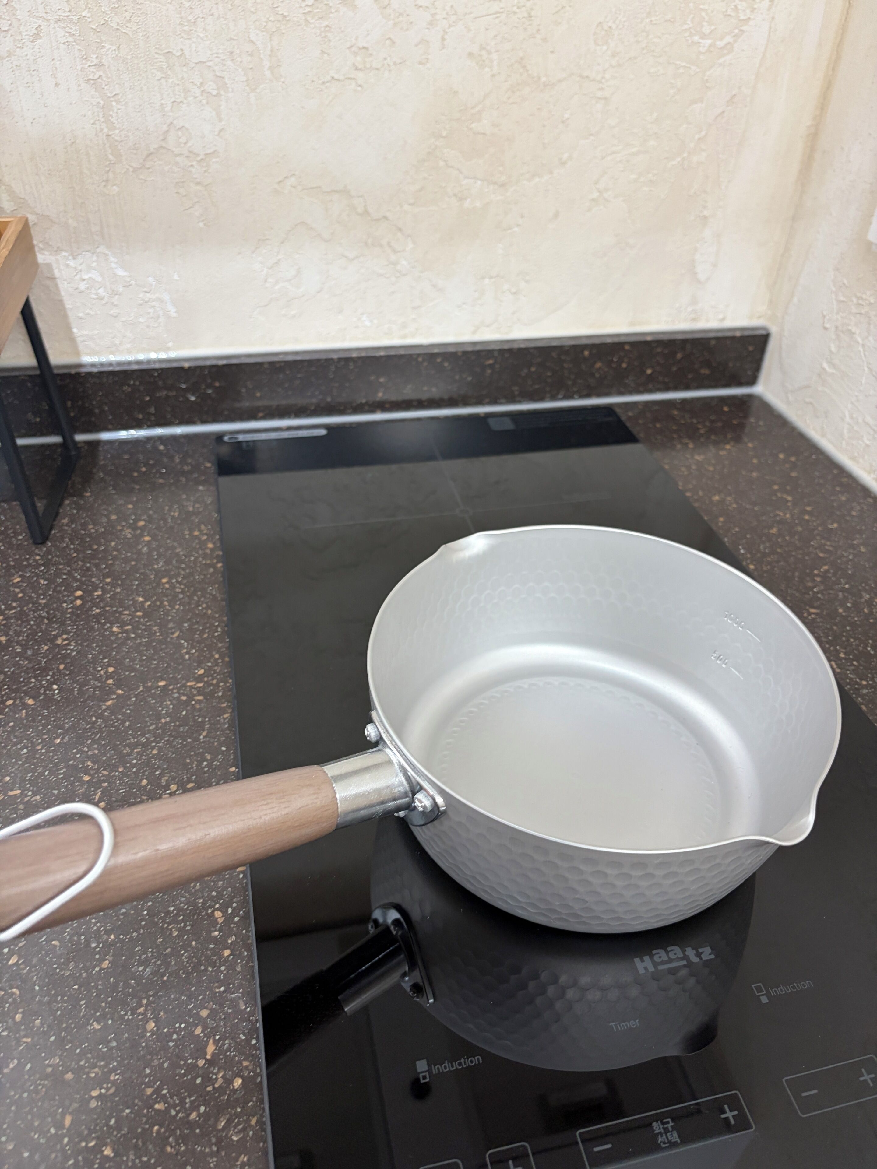 A kitchen with a black induction cooktop, a white non-stick frying pan with a wooden handle, and a black induction cooktop control panel.