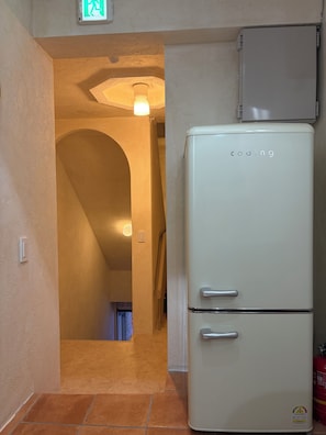 A compact kitchen with a white refrigerator, a tiled floor, and a hallway leading to another room. - StayDucksan Hotel (Suwon)
