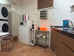 A compact kitchen with a washing machine, microwave, and a coffee machine. - StayDucksan Hotel (Suwon)