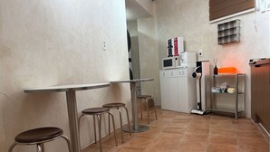 A kitchenette with a microwave, refrigerator, and a small shelf with glasses. There are two stools and a table. - StayDucksan Hotel (Suwon)