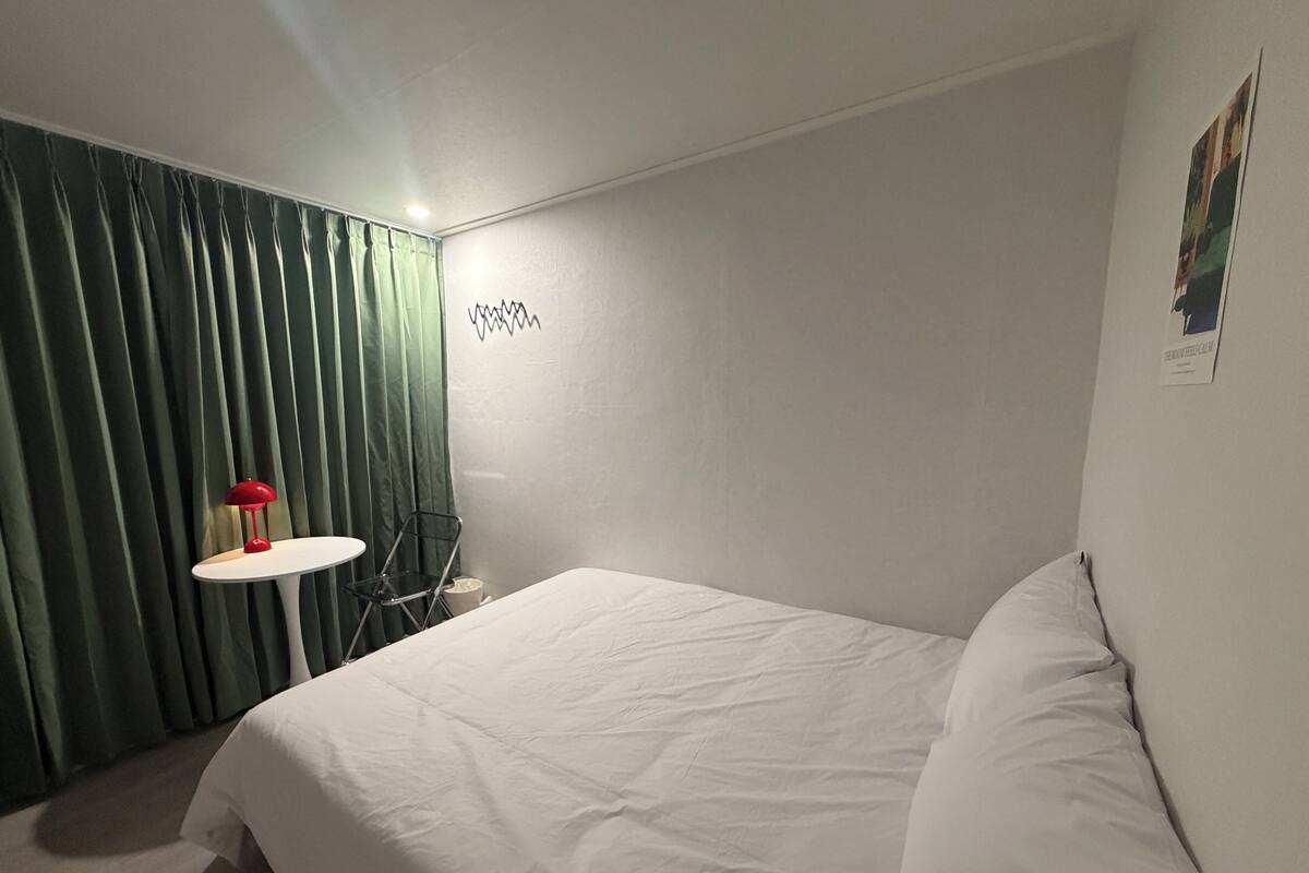 A bedroom with a bed, a small table with a lamp, a chair, and a wall-mounted sign.