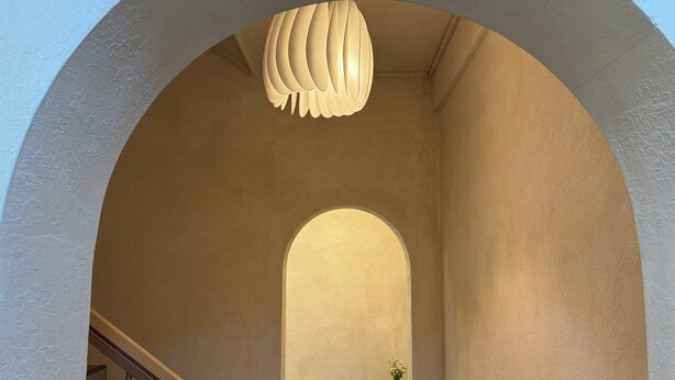 An arched hallway with a staircase on the left, a round table with a plant on the right, and a unique ceiling light fixture. - StayDucksan Hotel (Suwon)