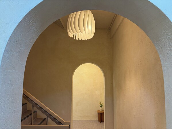 An arched hallway with a staircase on the left, a round table with a plant on the right, and a unique ceiling light fixture.