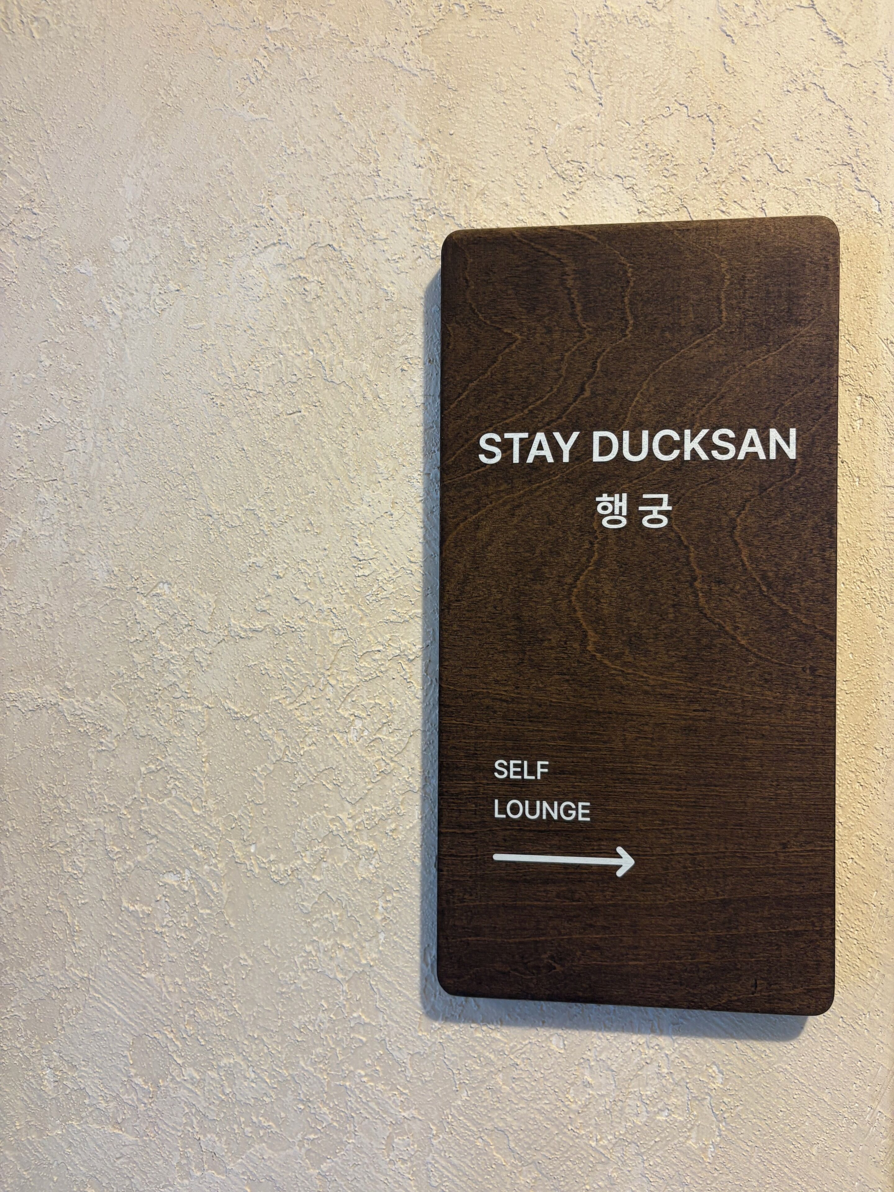 Un cartel con la leyenda 'STAY DUCKSAN' y 'SELF LOUNGE', que indica una zona de sala de espera con servicio propio.