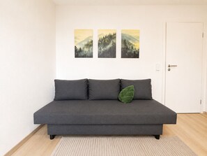 Un canapé gris avec un coussin vert, une porte blanche et trois tableaux représentant des paysages accrochés au mur.