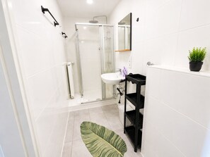 Une salle de bain moderne avec une douche à parois de verre, un lavabo blanc, un meuble de rangement noir et un tapis vert.