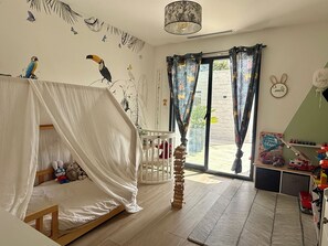Quarto de criança com cama, brinquedos, um papagaio de pelúcia pendurado e uma janela com cortinas.