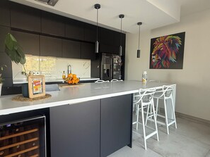 A modern kitchen with dark cabinetry, a large island, pendant lights, and a colorful abstract painting on the wall.