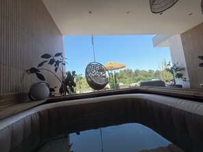 Un espace piscine intérieur moderne, agrémenté d’un fauteuil suspendu, d’une plante en pot et d’un parasol à toit de chaume.