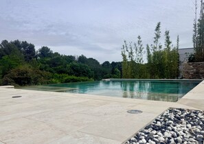 Une piscine rectangulaire, bordée d’une terrasse carrelée et entourée de verdure et de bambous.