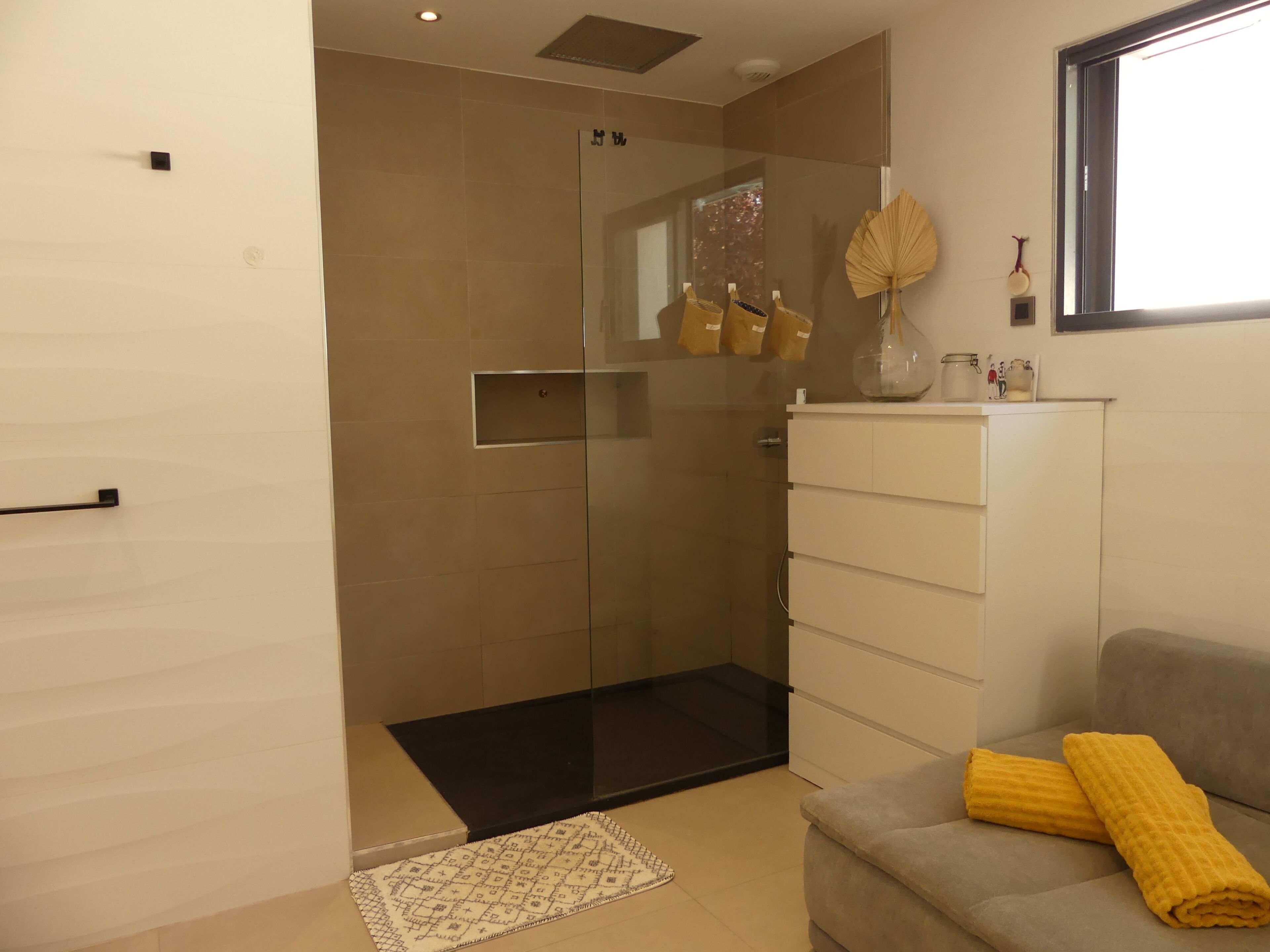Ein modernes Badezimmer mit Duschkabine aus Glas, einem weißen Schrank und einem grauen Sofa mit gelbem Handtuch.
