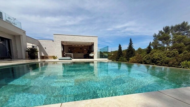 Ett modernt hus med en swimmingpool, en möblerad uteplats och utsikt över träd.