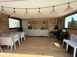 Cozinha e sala de jantar integradas, com forno de tijolos, piso de madeira e luzes de cordão.