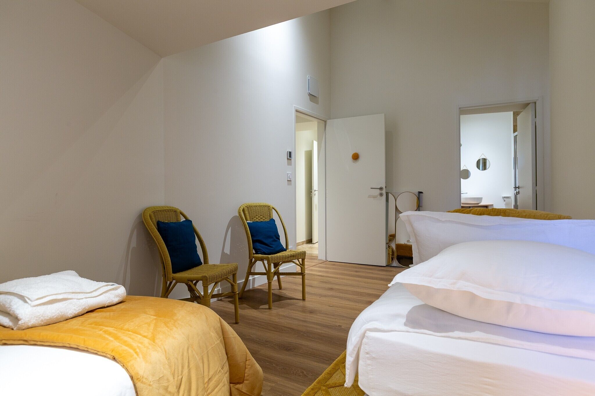 A hotel room with two beds, a chair, a door, and a mirror.