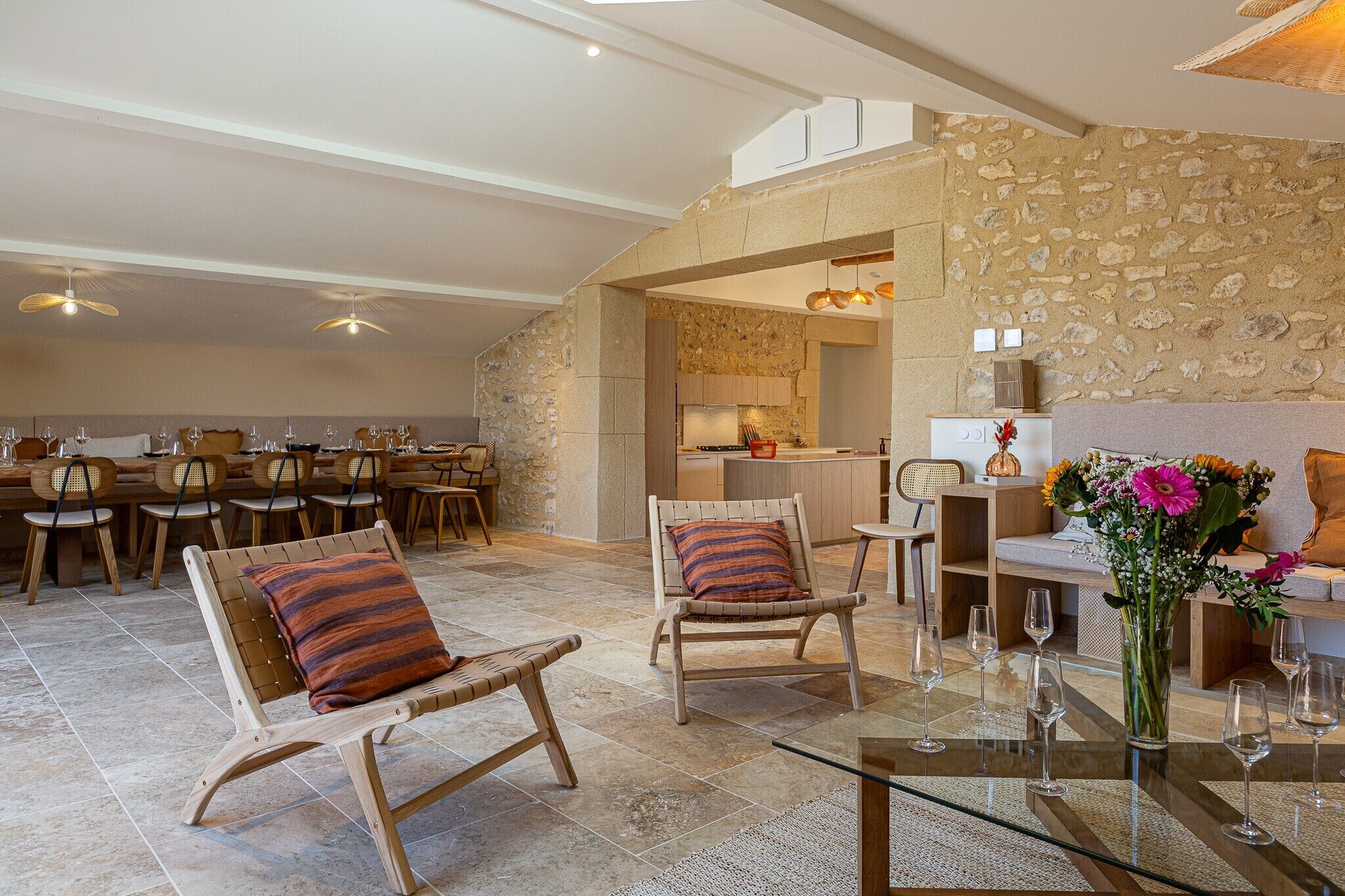 A spacious living area with a dining table, two rocking chairs, a glass coffee table, and a stone wall.