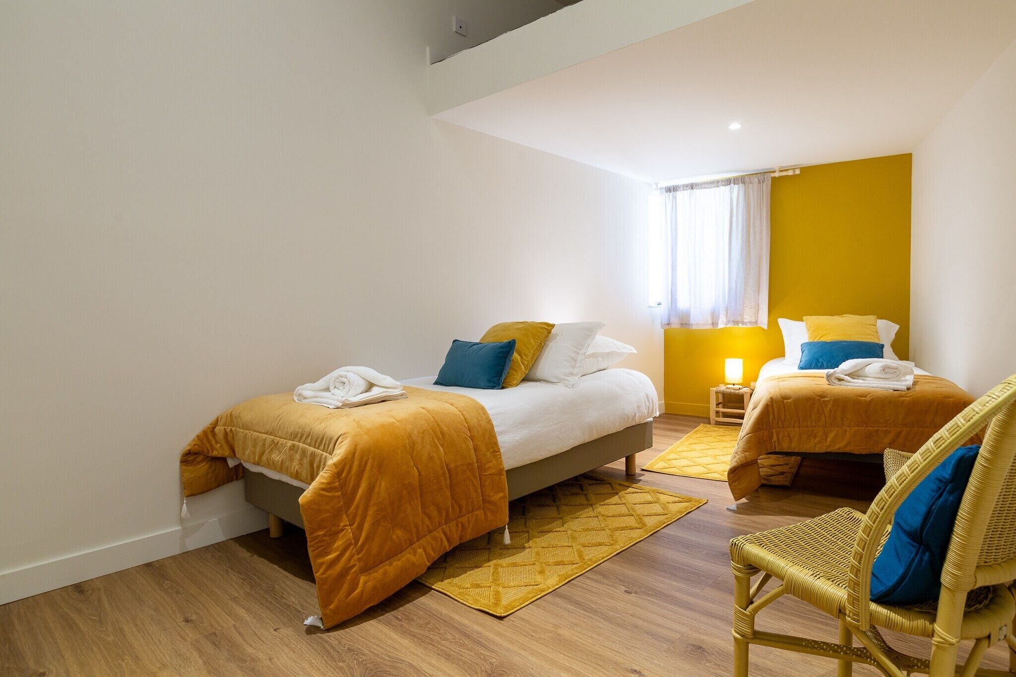 Ein Hotelzimmer mit zwei Betten, einer gelben Akzentwand und einem Korbstuhl.