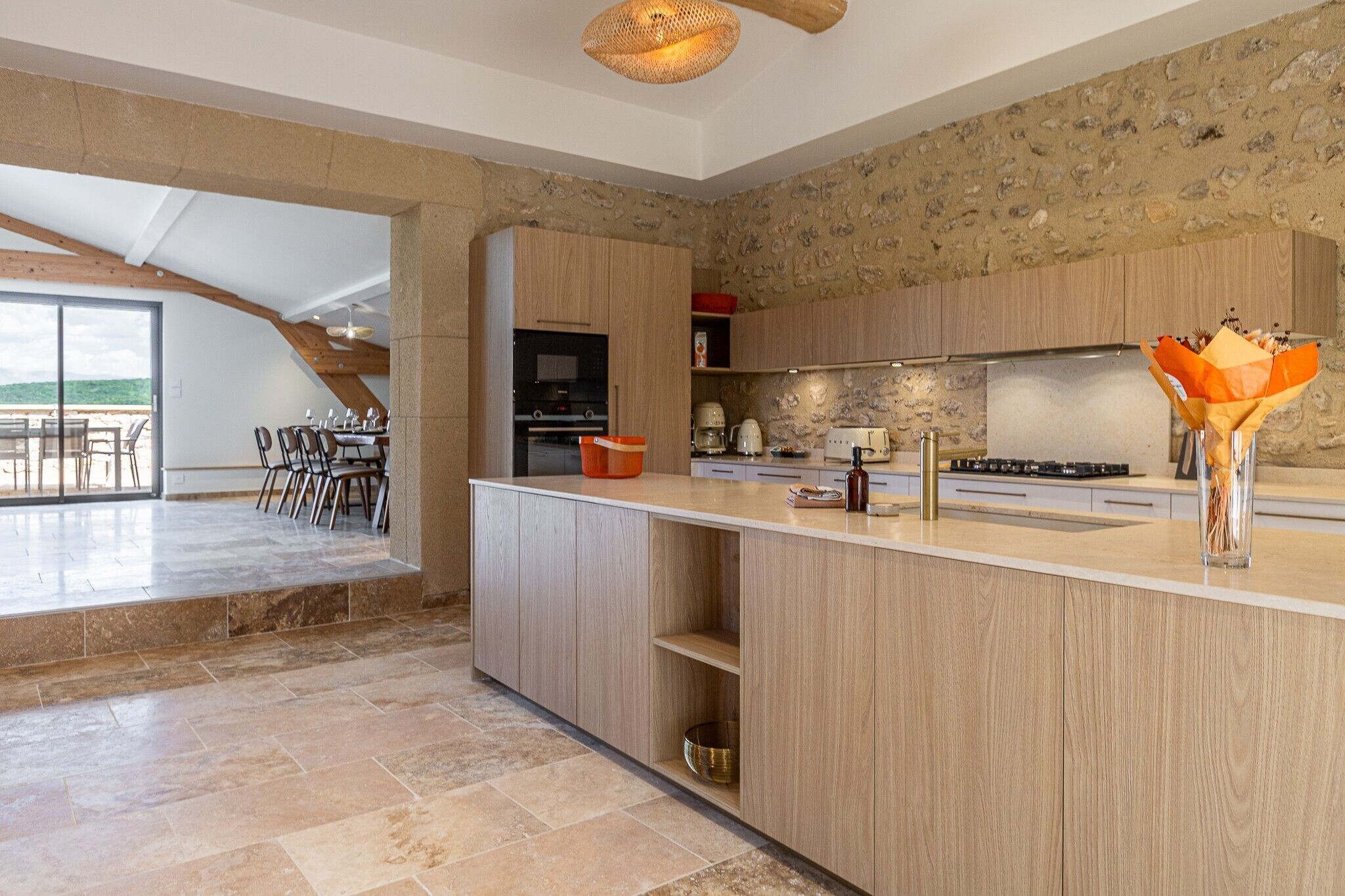 A modern kitchen with a stone wall, wooden cabinets, and a dining area with a view.