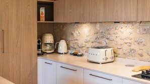 Eine Küche mit weißen Schränken, einer Steinrückwand, einem Toaster, einer Kaffeemaschine und einem Regal mit Orangensaft.