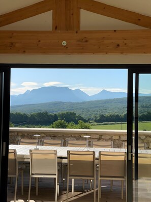 A room with a view of mountains, a stone wall, and a table with chairs.