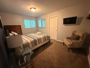 Un dormitorio con cama, una silla, televisor y ventana.