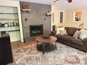 A living room with a stone fireplace, a brown sofa, a coffee table, and a bookshelf with books.