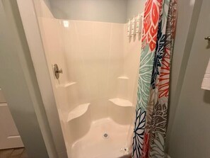 Eine Dusche mit weiß gefliester Wand, einem Duschvorhang mit Blättermotiv und einem sichtbaren Ablauf.