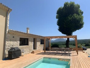 A pool area with a pergola, outdoor seating, and a view of mountains.