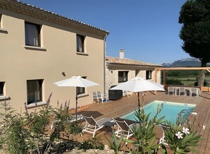 A pool area with lounge chairs and umbrellas, a building with multiple windows, and a view of a mountainous landscape.