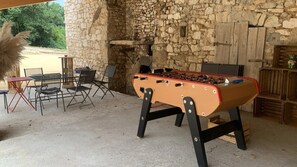 Un mur en pierre, un espace extérieur aménagé avec des chaises et une table, et une table de baby-foot.