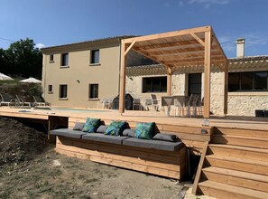 A wooden deck with a sofa and cushions, a pool, and a covered outdoor seating area.