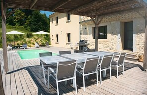 A wooden deck with a pool, outdoor seating, and a stone building in the background.
