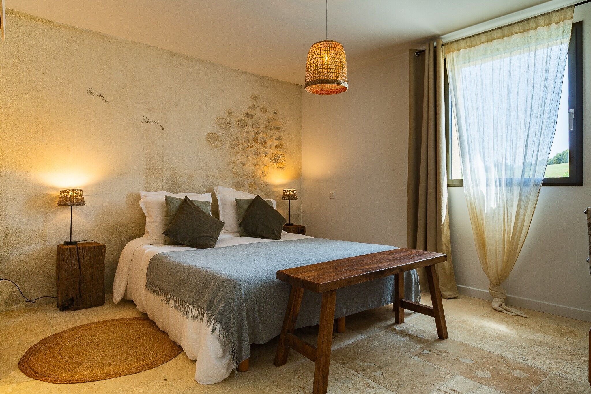 Ein Schlafzimmer mit Bett, Nachttischlampen, einer Holzbank, einem Teppich und einem Fenster mit Vorhängen.