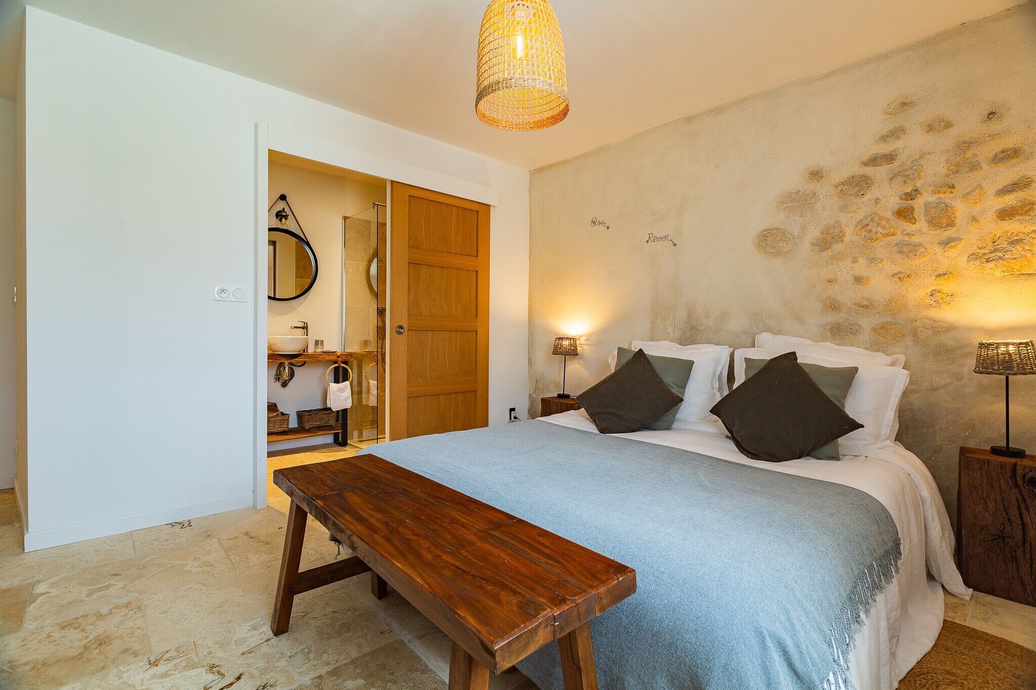 Ein Schlafzimmer mit einem Holzbett, einer Bank, einem Nachttisch und einer Wand mit strukturierter Oberfläche.
