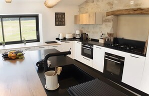 Une cuisine moderne avec des meubles blancs, un plan de travail noir et une vue sur lâextĂ©rieur grĂące Ă une grande fenĂȘtre.
