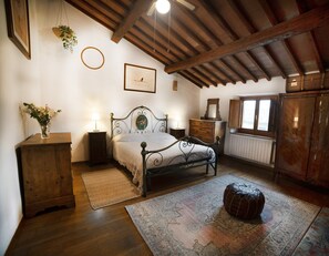 A bedroom with a wooden ceiling, a bed with a metal frame, a wooden dresser, a nightstand, a hanging plant, and a window with a view. - Poetic Florence - Spacious Central Home: 3-BR, 2-Bath, Lift, View & Parking (Firenze)
